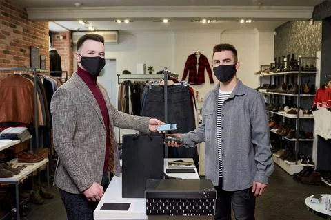 Man in a face mask is using a smartphone to pay by NFC for purchases in a sto Stock Photos