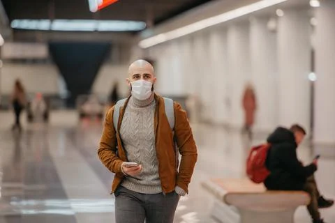 A man in a face mask is using a smartphone while waiting for a subway train. Stock Photos
