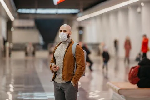 A man in a face mask is using a smartphone while waiting for a subway train. Stock Photos