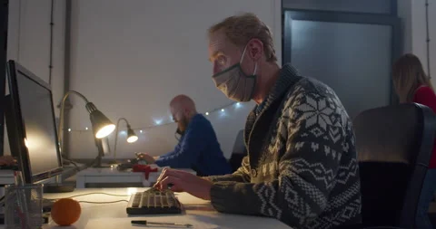 Man in face mask working on computer at desk at night Video stock 144270990
