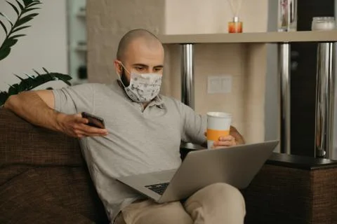 A man in a face mask working remotely on his laptop during the quarantine. Stock Photos