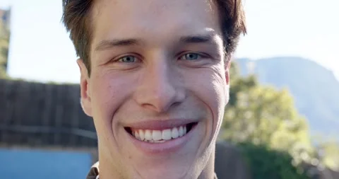 Man facing camera, holding gaze while smiling, revealing teeth in backyard, Vídeo Stock 342032446