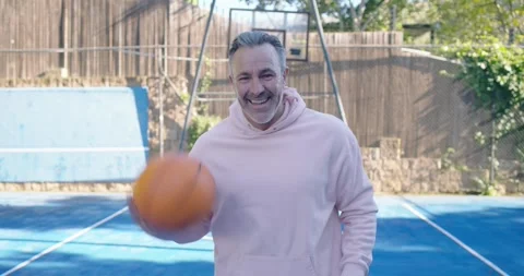 Man facing camera in pink hoodie, dribbling orange basketball on backyard court, Vídeos de archivo 342084659