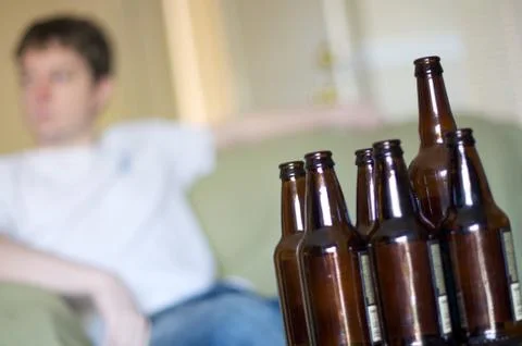 Man facing left with group of empty beer bottles, angled Stock Photos