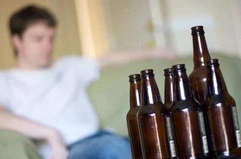 Man facing right at a group of empty beer bottles, angled Stock Photos