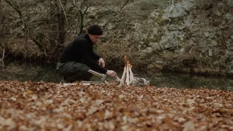 Man in the fall by the river makes a fire in the forest Stock Footage 317215020