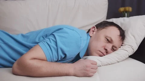 Man falls on a cozy light sofa and falls asleep, concept of relaxation after a Stock Footage 162216640