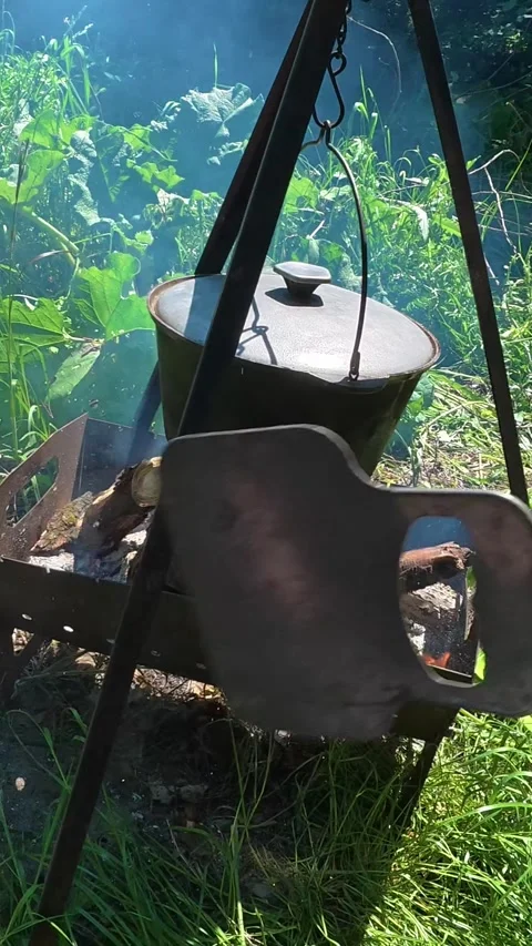 Man fanning campfire with cauldron pot hanging Video stock 337940993