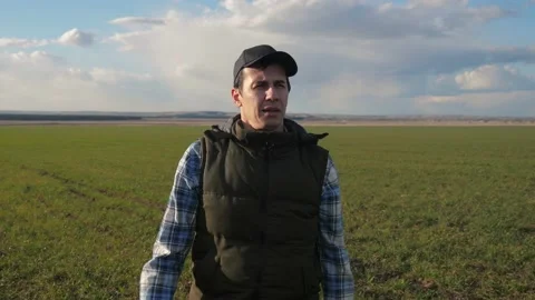 Man farmer red neck in a cap is walking on a green field. spring harvest Stock Footage 136459737
