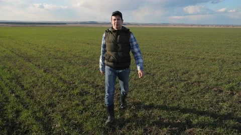 Man farmer red a neck in cap is walking on a green field. spring harvest Video stock 136459868