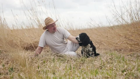 A man farmer in a straw hat sits on the field and strokes the dog smiling Stock Footage 190527933