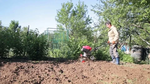 A man is a farmer in a suburban area, a vegetable garden, plows the land with Stock Footage 79892085