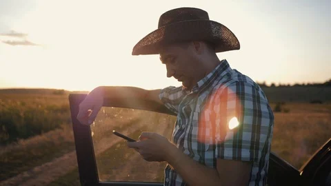 A man-farmer is wearing a hat at sunset and is working on a smarphone Stock Footage 101482854