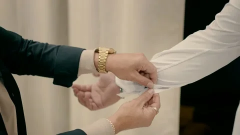 Man fastens a button on the sleeve of a white elegant shirt of other man. Video stock 225640227