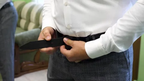 A man fastens his belt on his pants. Stylish men's clothing. Vidéo 312317618