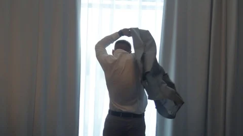 Man fastens suit by the window, view from the back Stock Footage 122234687