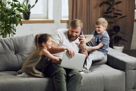 Man, father sitting on couch, talking on phone and working on laptop in living Stock Photos