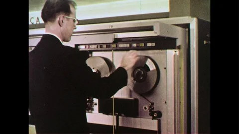 A man feeds the magnetic tape into a computer which is processed by a console Stock Footage 74452048