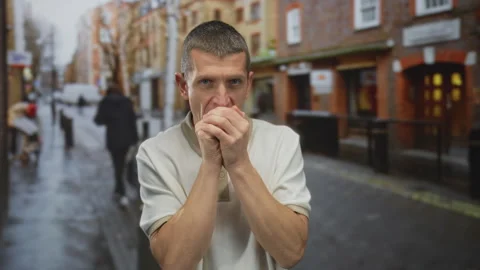 Man feeling cold on a wet street with hands clasped, wearing a light shirt,.. Vídeo Stock 312801233