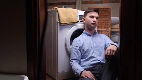 Man feeling exhausted and sad while waiting for the washing machine cycle to Stock Footage 324768575