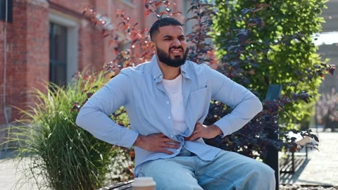 Man feeling sudden sharp pain in stomach while relaxing on bench with cellphone Stock Footage 250077581
