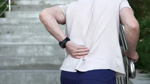 A man feels a sharp pain in his lower back and massages his back. Stock Footage 253635737