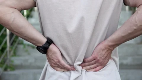 A man feels a sharp pain in his lower back and massages his back during exercise Stock Footage 254412941