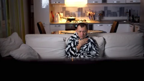 The man fell ill, in the evening on the sofa sits wrapped in a plaid Stock Footage 132449390
