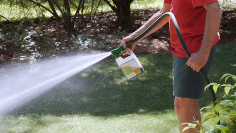 Man fertilizing residential backyard lawn with liquid chemical spreader. Stock Footage