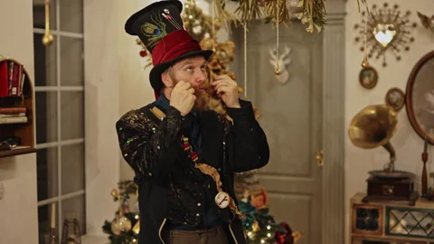 Man in Festive Costume with Top Hat Adjusting Mustache On Christmas Decor Stock Footage 293014273
