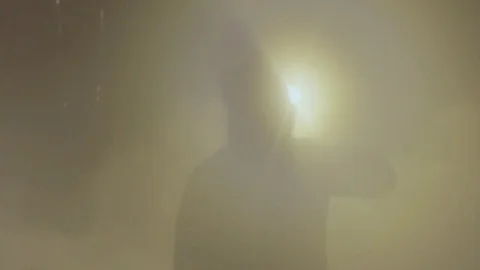 Man figure in hooded jacket stand in white steam cloud blocking light beam Stock Footage 73054140