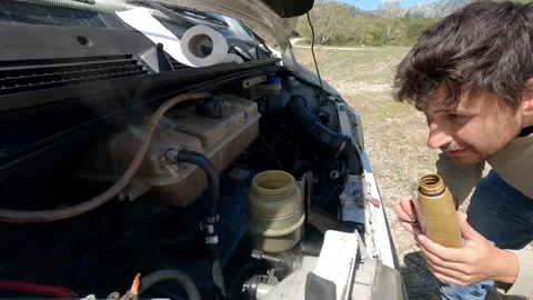 Man filling engine oil during a camper van maintenance in the outdoors Stock Footage 322685595