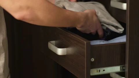 A man fills an empty shelf with folded clothes, close-up, side view Stock Footage