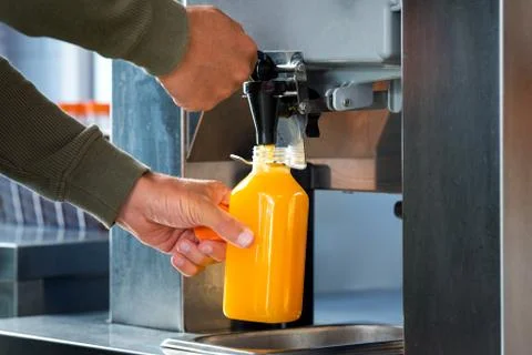 Man fills a plastic bottle with squeezed orange juice from a juicer in Stock Photos