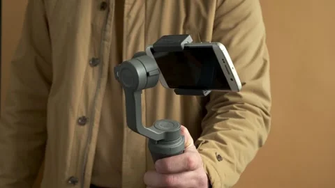 Man filming with a smartphone using a gimbal stabilizer on yellow background. Video stock 251022798