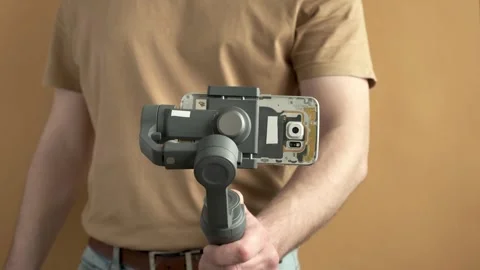 Man filming with a smartphone using a gimbal stabilizer on yellow background Stock Footage 315136408
