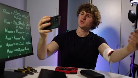 Man films glowing wearable sensor while checking live data in tech lab Stock Footage 324443684