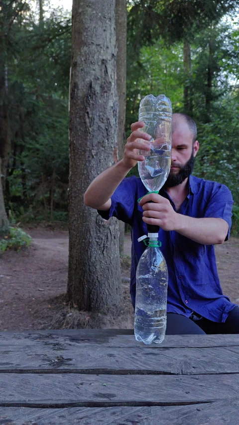 Man Filtering Water Between Plastic Bottles at Forest Campsite 動画素材 345065826