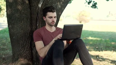 Man finish using laptop while sitting under the tree and relaxing Stock-Footage 69964912