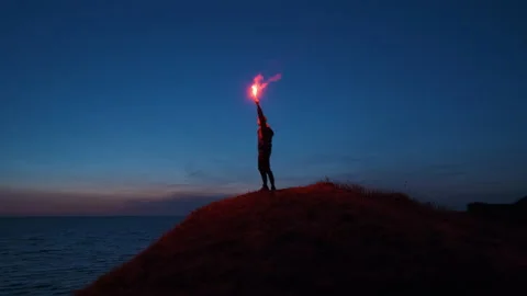 The man with a fire stick standing on the mountain top near the sea. slow motion Video stock 144041213