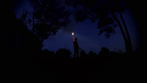 A man with a firecracker stick stands in the middle of the woods at night Stock Footage 214836354