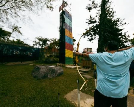 A man is firmly pulling the string of a big bow in an extreme park. Stock Photos