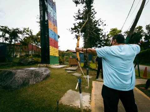 A man is firmly pulling the string of a big bow in an extreme park. Stock Photos