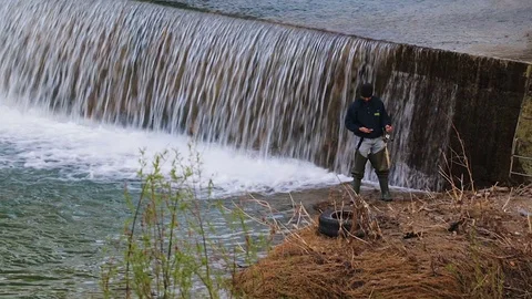 Man fishing in the river and checking the phone Stock Footage 76329308