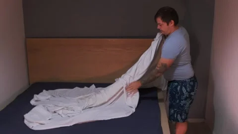 Man fitting a bedsheet on a mattress, stretching fabric evenly and smoothing Stock Footage 333578768