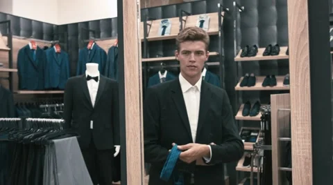 The man in the fitting room, looking in the mirror corrects tie in shop Video stock 66428142