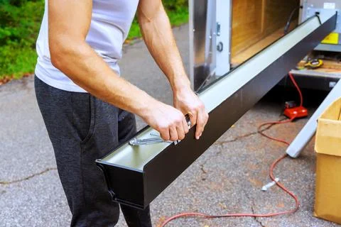 Man fixes gutter channels while standing beside trailer Stock Photos