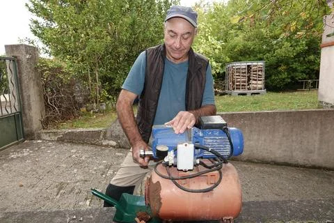 Man fixes a motor while working in his yard on a sunny day Stock Photos