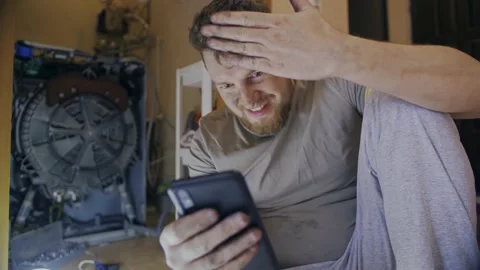 A man fixes a washing machine and watches instructions on his phone Stock Footage 155337575