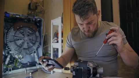 A man fixes a washing machine and watches instructions on his phone Stock Footage 155337675